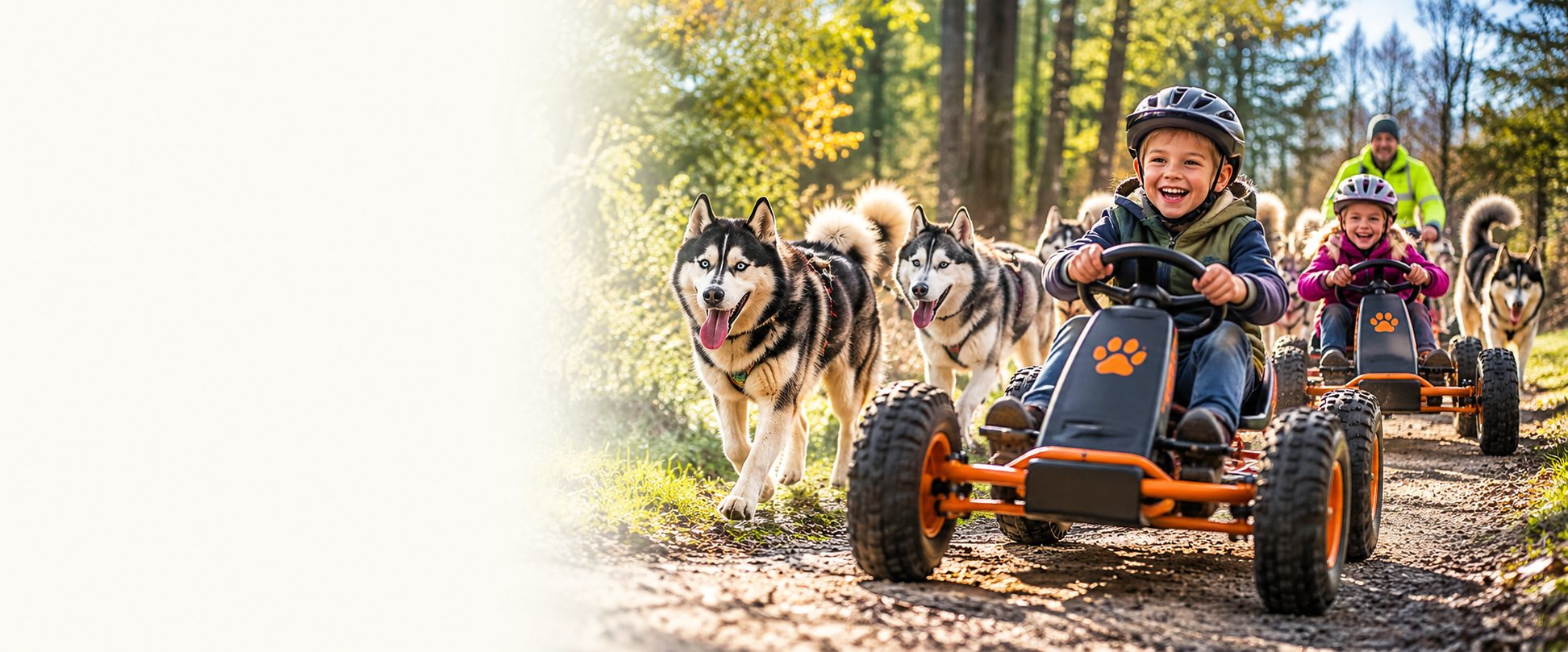 Kinder fahren mit Pedal-Kett-Karts durch den Wald, Huskys laufen nebenher