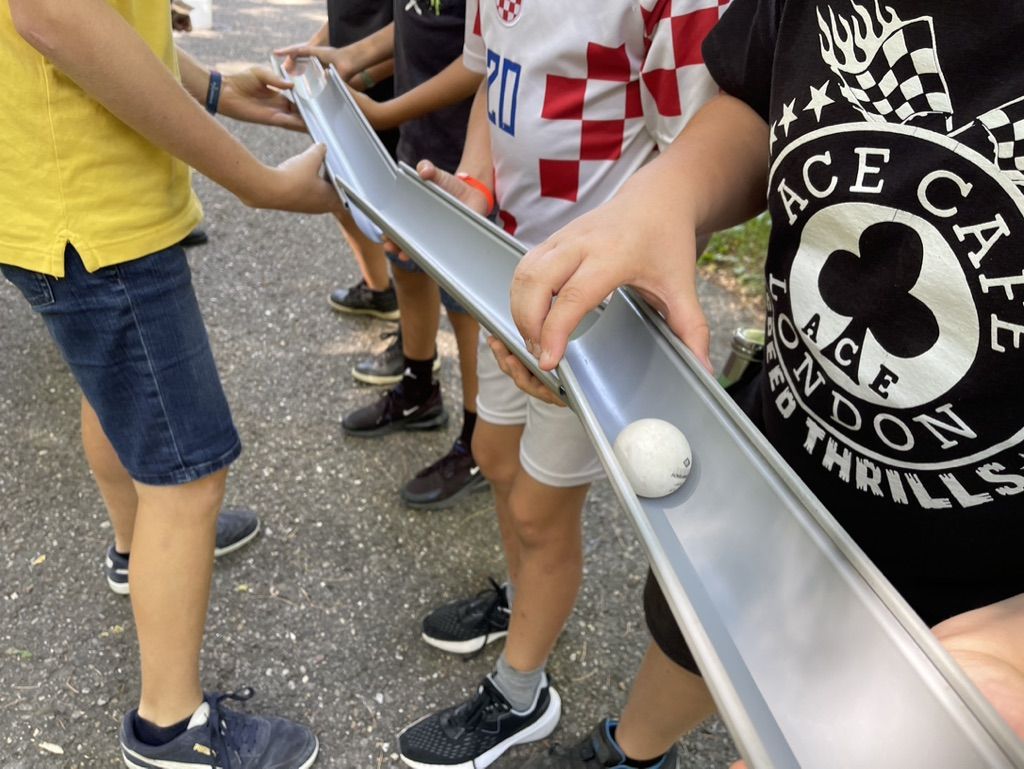 Kinder bringen gemeinsam eine Kugel über eine lange Rinne ans Ziel